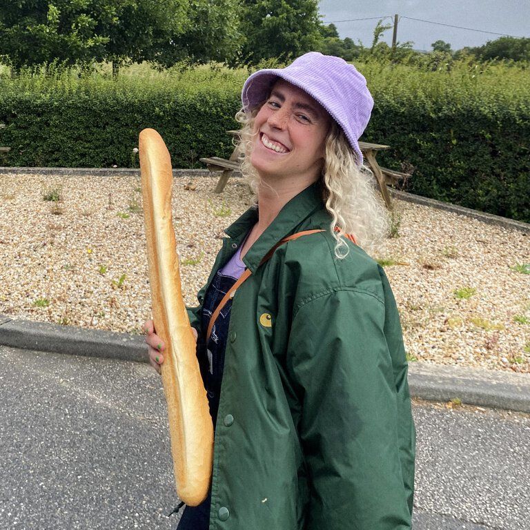 Ein Mitarbeiterin der CASTENOW GmbhH trägt ein Baguette in der Hand und einen rosa Hut.