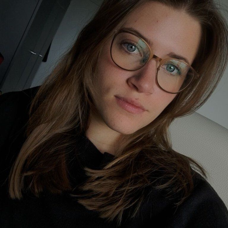 Talia Hinz, Mitarbeiterin der Castenow GmbH, trägt einen schwarzen Pullover, eine Brille und lange dunkelblonde Haare.