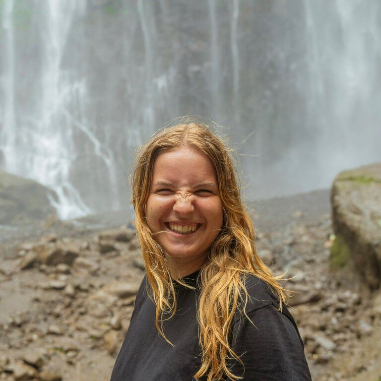 Malina Riefke, Mitarbeiterin der Castenow GmbH, steht mit nassen Haaren lachend vor einem Wasserfall.